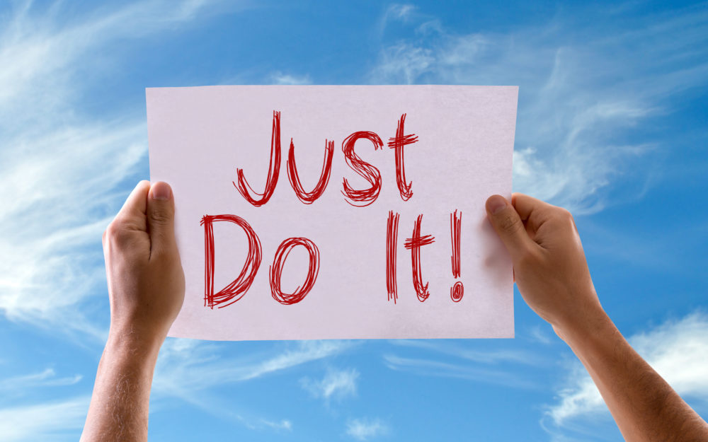 Person hält motivierendes "Just do it"-Schild nach oben, vor blauem Himmel