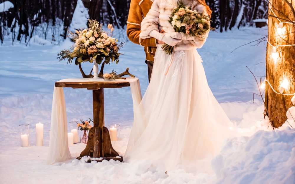 Hochzeitspaar im Schnee im Freien mit winterlicher Dekoration und weißem Brautkleid
