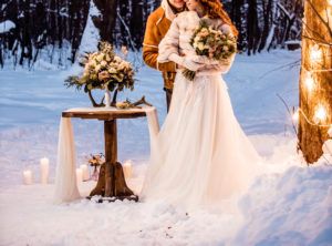 Hochzeitspaar im Schnee im Freien mit winterlicher Dekoration und weißem Brautkleid