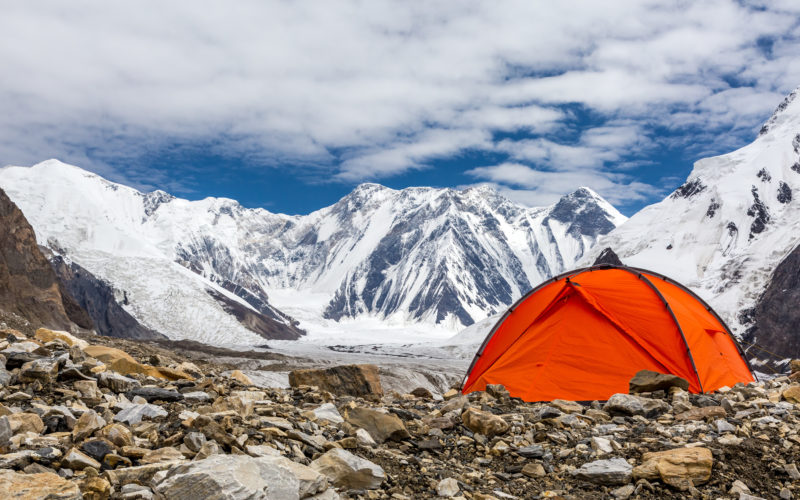 Ein rotes Zelt auf steinigem Boden auf einem Berg mit Gletschern im Hintergrund.
