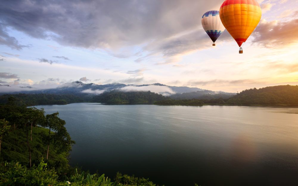 Blick auf einen See in der Abenddämmerung mit zwei Heißluftballons am Himmel