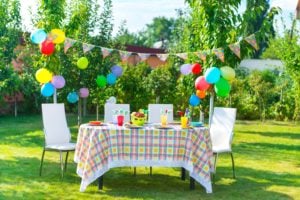 Gedeckter Tisch mit Dekoration aus Wimpeln und Luftballons zum Geburtstag auf einer grünen Wiese im Freien
