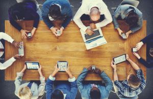 Menschen mit Laptops, Tablets und Smartphones sitzen um einen Tisch herum, Blick von oben
