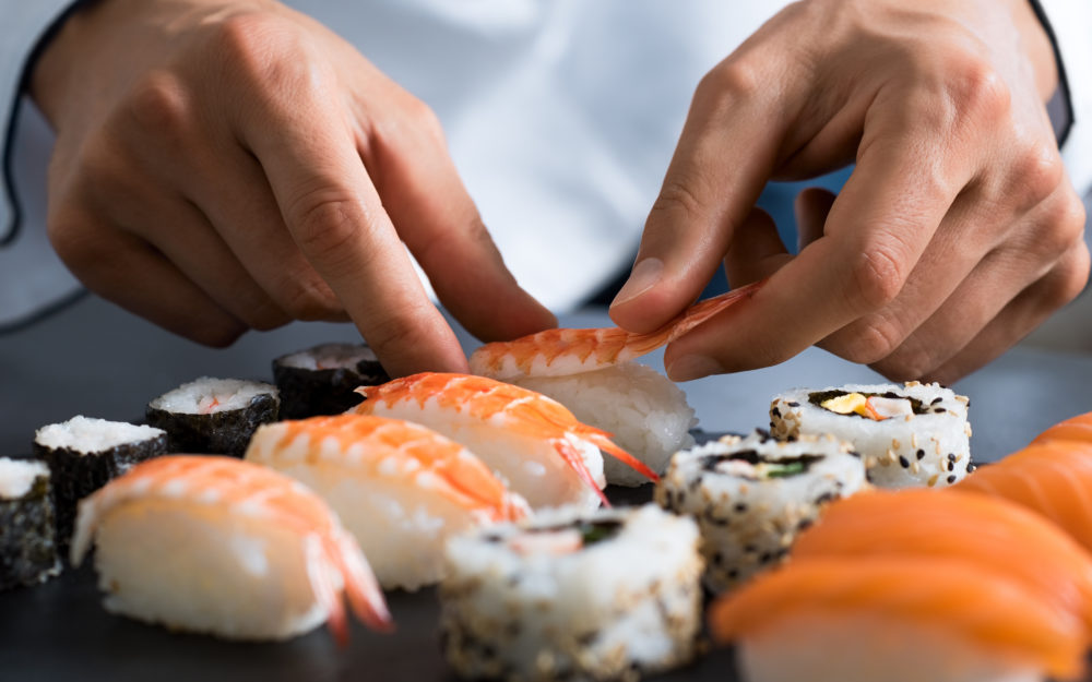 Verschiedene Sushirollen auf einem Tisch, die gerade frisch zubereitet werden