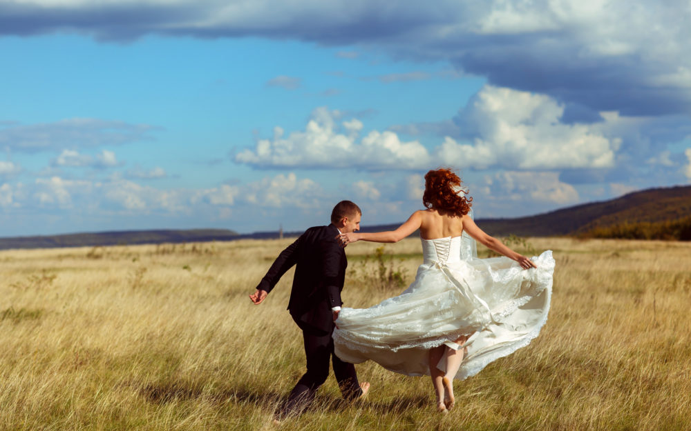 Glückliches Hochzeitspaar nach der Trauung im Freien, springend auf einem Feld