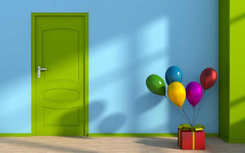 Blauer Raum mit grüner Tür, in dem eine Geschenkbox steht, an die Luftballons gebunden sind