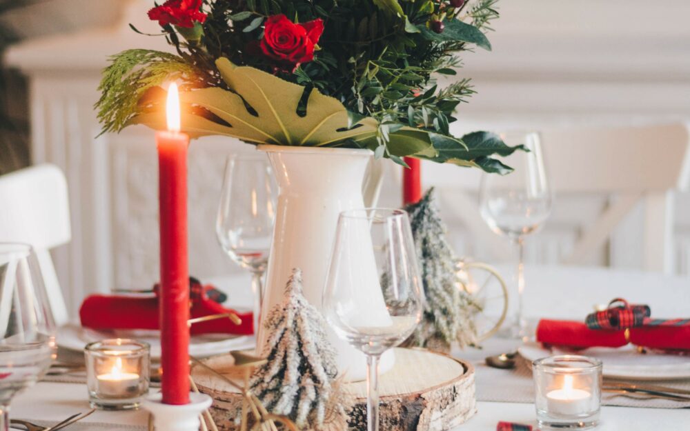 Festlich gedeckter Essenstisch mit weihnachtlichen Dekoelementen, Kerzen, rotem Farbschema und einem Blumenstrauß in der Mitte.