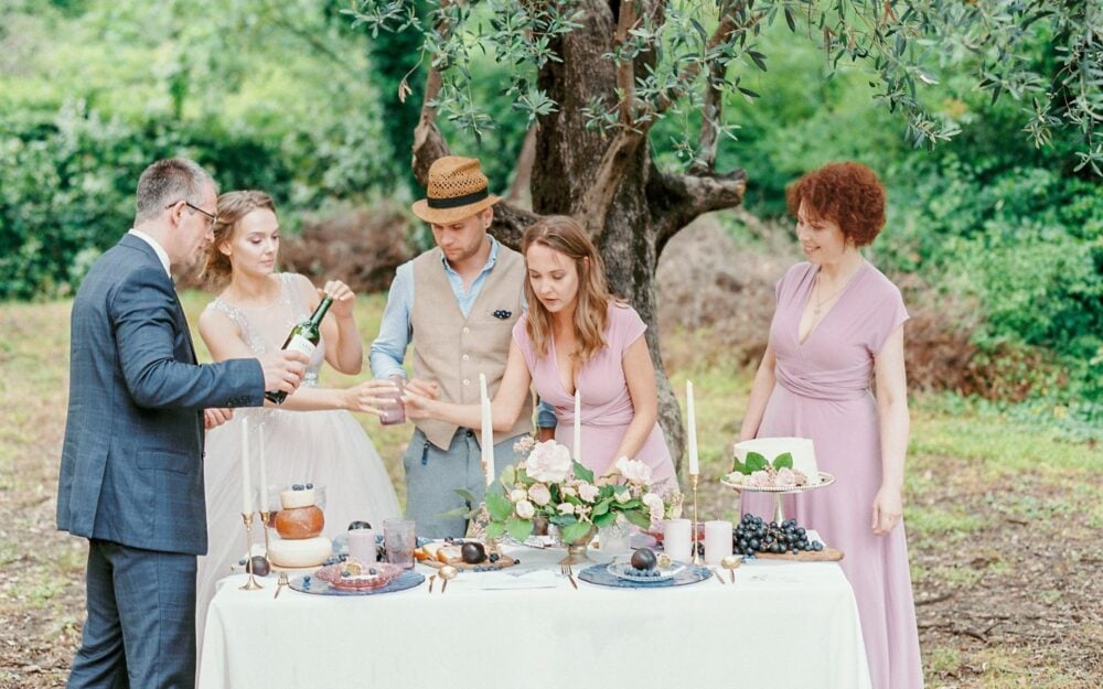 Ein Brautpaar feiert Hochzeit mit der Familie im Garten, sie stehen an einem Tisch mit Blumen und Lebensmitteln