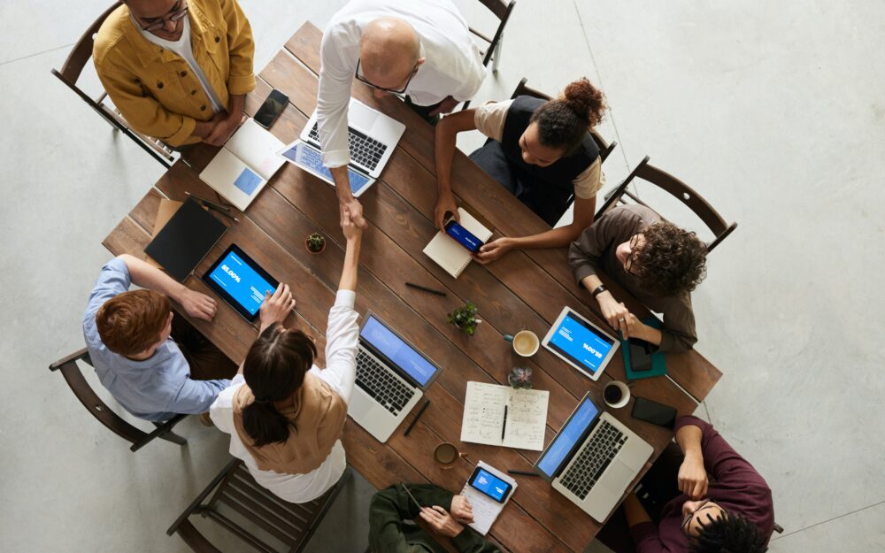 Ein von oben fotografiertes Bild, welches 8 Kollegen zeigt, die gemeinsam an einem Tisch sitzen und mithilfe von Laptops und Schreibmaterialien arbeiten