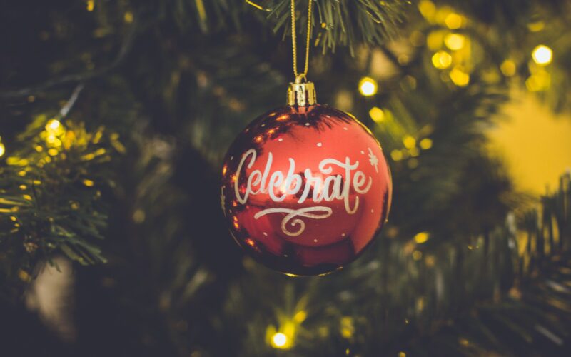 Eine Weihnachtskugel mit der Aufschrift "celebrate" hängt an einem Weihnachtsbaum