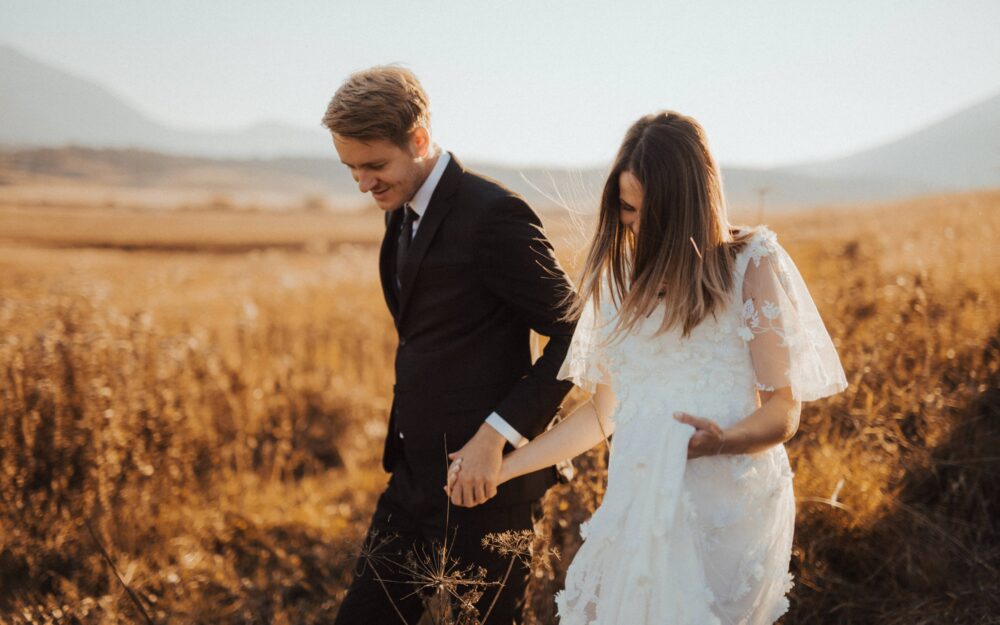 Ein Brautpaar läuft lachend durch ein Feld bei einer freien Hochzeit