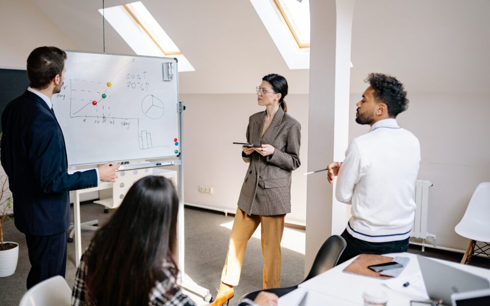 Vier Personen stehen in einem Büro vor einem Whiteboard und arbeiten gemeinsam an einem Projekt