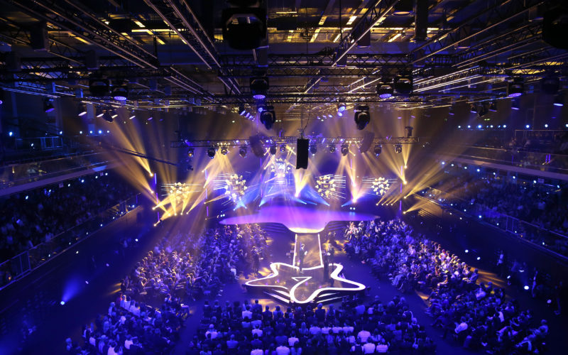 Eventlocations für bis zu 1000 Personen in Düsseldorf - Lila beleuchtete Halle mit vielen Menschen auf den Sitzplätzen