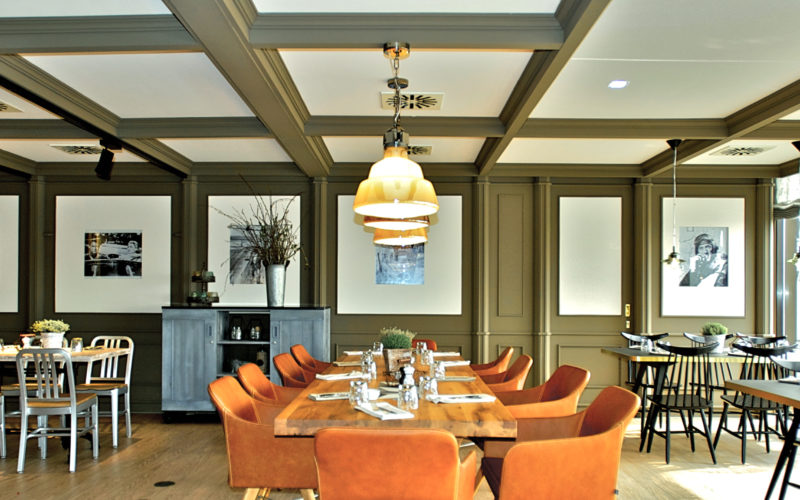 Raum mit Holzbalken und zentralem Tisch mit orangenen Stühlen