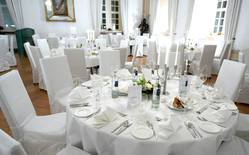 Festlich eingedeckte Tische in weiß und Stühle mit weißen Hussen