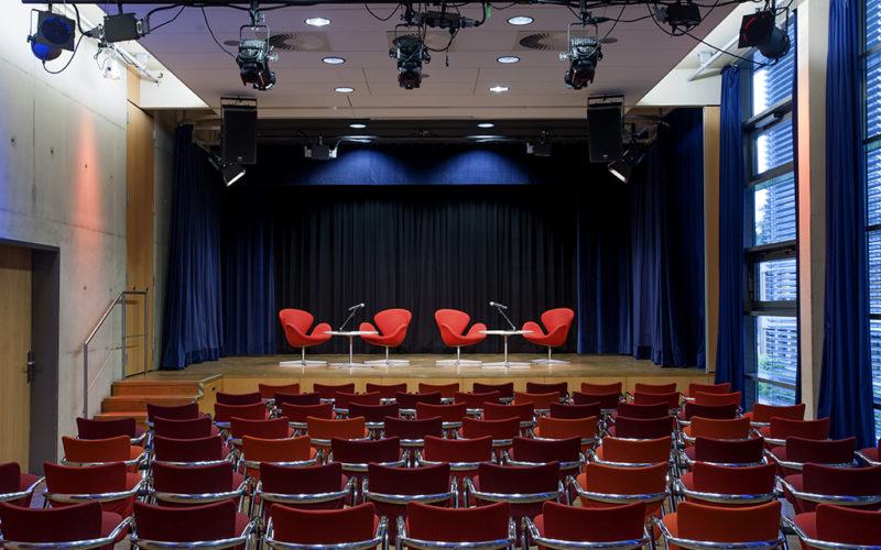 Saal mit roten Stühlen und einer Bühne
