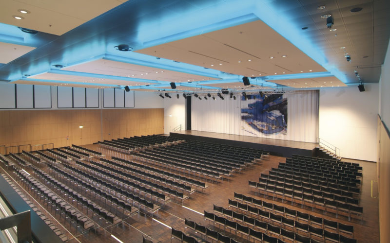 Großer Konferenzsaal mit vielen schwarzen Stühlen und blauer Beleuchtung