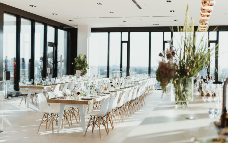 Gedeckte Tischreihe mit weißen Stühlen vor Fensterfront; Eventlocations für bis zu 200 Personen in Düsseldorf