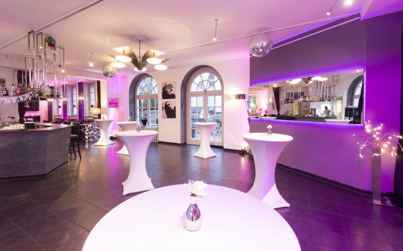 Empfangsbereich mit Stehtischen, hochwertigen Desingelementen und bestrahlt mit lila Licht, Firmenfeier in Aachen