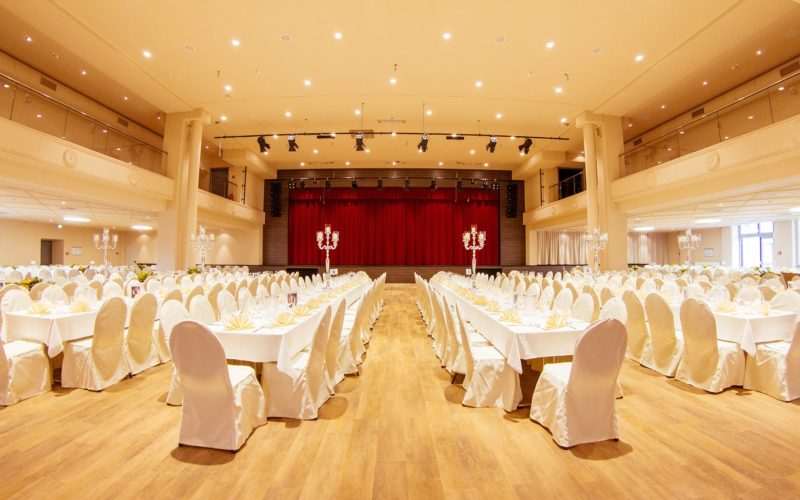 Große Eventhalle mit einer Bühne und vielen Tischen und Stühlen