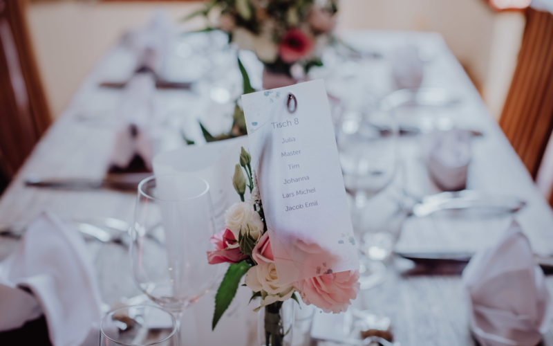 Nahaufnahme eines weiß dekoriertem Hochzeitstisch mit Blumen