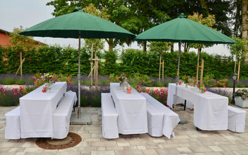 Hochzeitslocation in Grevenbroich - Weiße lange Tische mit Sitzen unter grünem Regenschirm