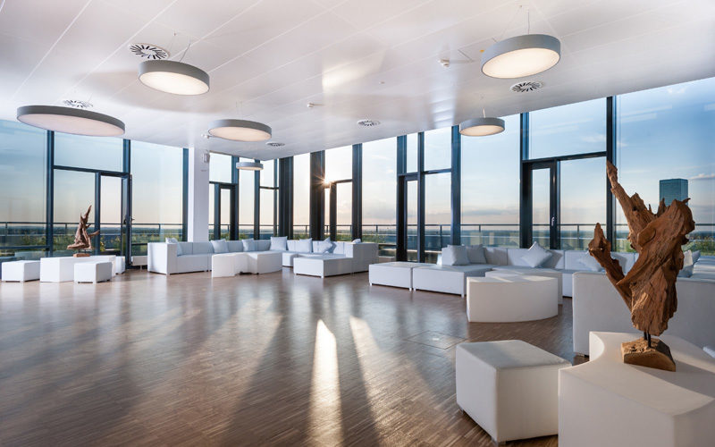 Großer, lichtdurchfluteter Raum mit Glaswänden und stilvollen, weißen Loungemöbeln; Rooftop Locations in München