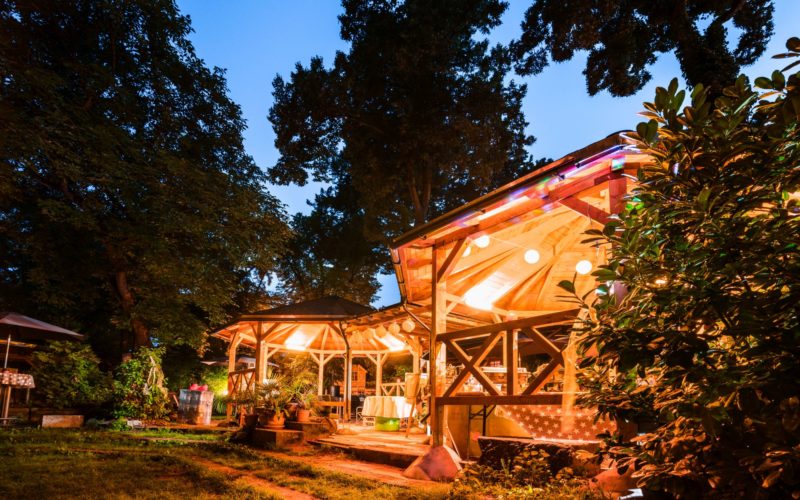 Gemütlicher Eventgarten mit überdachten Holzpavillons und Lichterketten; Party in Potsdam