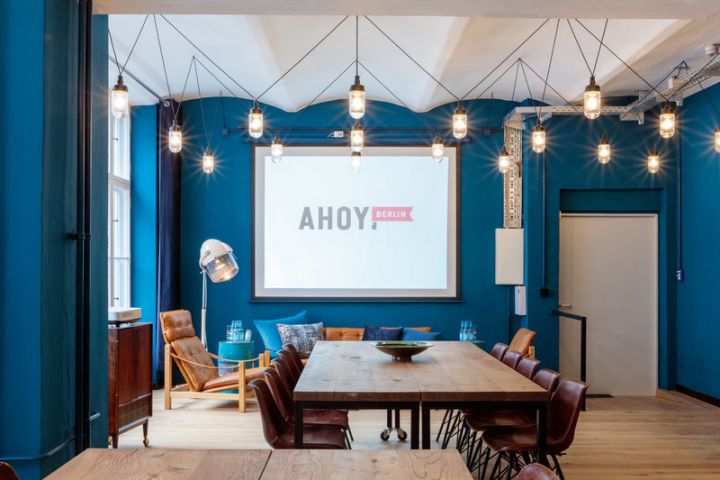 Meetingraum mit blauen Wänden, einer Leinwand, Holztisch und Stühlen