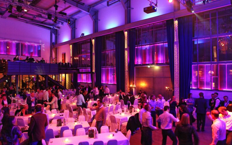 Eventlocation in großer industrieller Halle mit Tafelbestuhlung im pinken Licht, Firmenfeier in Bottrop: Finden Sie die perfekte Eventlocation!