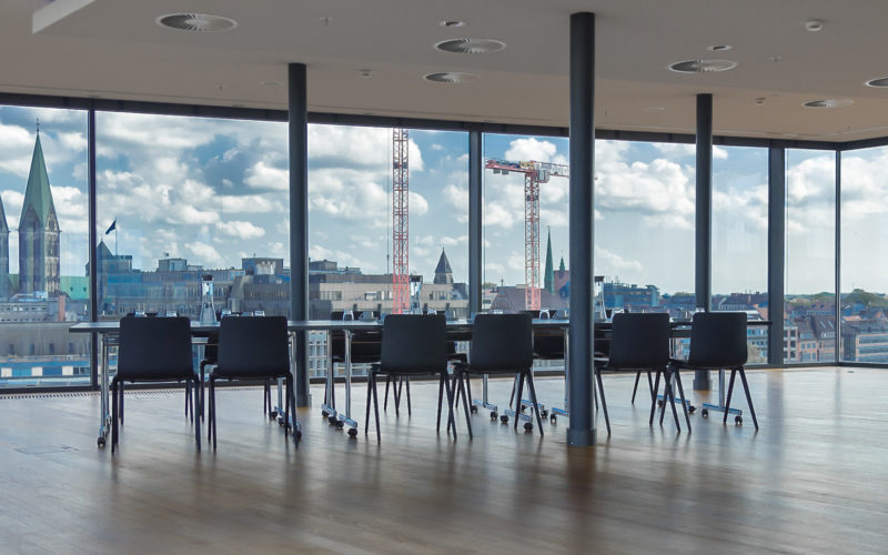 Eventlocation mit Fensterwänden und Aussicht über die Bremen. In der Mitte befindet sich ein modernen Tisch mit Stühlen, Traumhafte Firmenfeier in Bremen