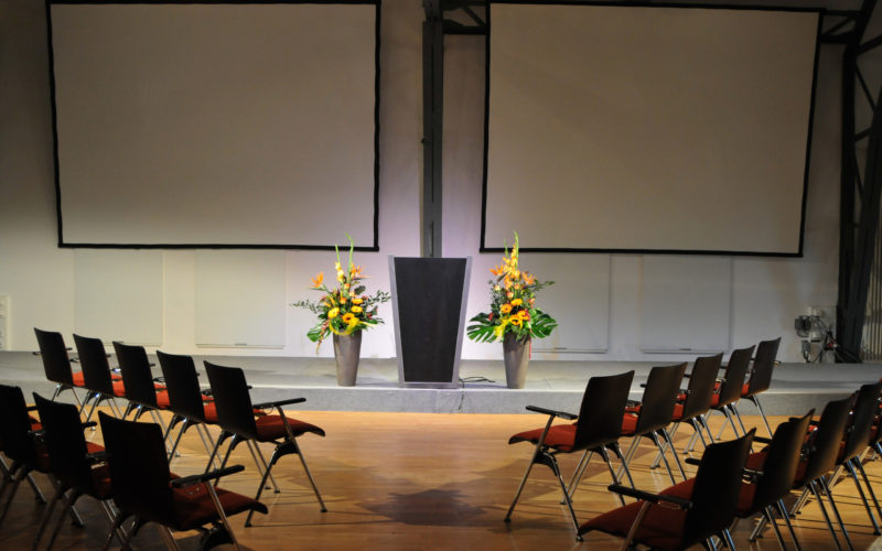Konferenzlocation mit Stühlen die auf ein Podium gerichtet sind