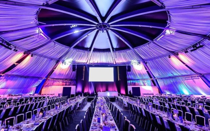 Große Eventhalle mit Lichttechnik, einer Bühne, Tischen und Stühlen