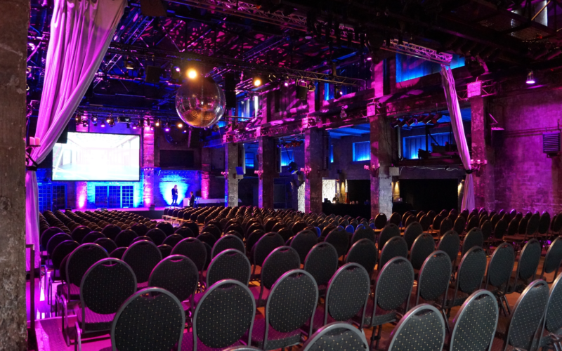 Location mit Reihenbestuhlung vor einer Bühne im dunklen Design mit pinken Lichthighlights; Messehalle in Aachen