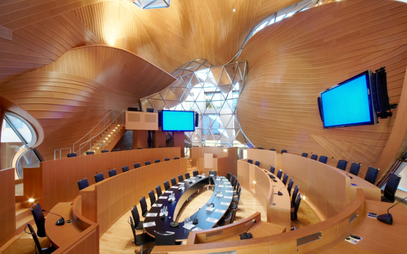 Moderne Architektur mit geschwungenen hellen Holzwänden und einem ovalen Besprechungstisch in der Mitte; Messehalle in Berlin