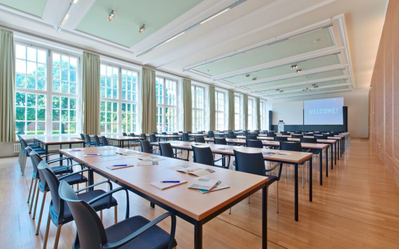 Heller Raum mit bodentiefen Fenster in dem sich bestuhlte Tischreihen mit Blick auf eine Leinwand befinden; Messehalle in Bremen