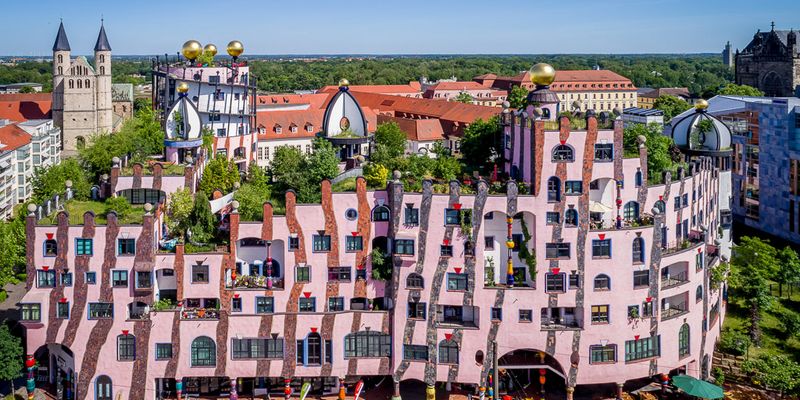 Produktpräsentation in Magdeburg - Verrücktes rosa-farbenes Haus mit unterschiedlich hohen Fenstern und Blumen auf dem Dach