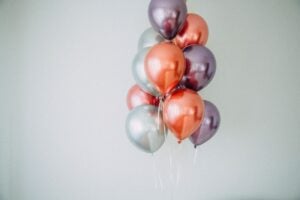 Ballons in metallischem Rot, Lila und Grau schweben zusammengebunden vor einer weißen Wand