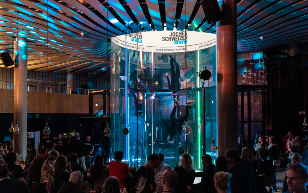 Die Deutsche Indoor Skydiving Weltmeisterschaft findet inmitten eines Publikums statt, welches sich um den Windkanal, geschützt durch Glas, versammelt hat