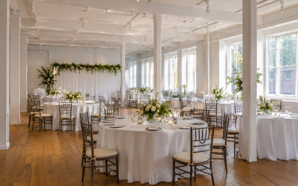 Helle Eventlocation mit gedeckten runden Tischen, Blumen und natürlichem Licht