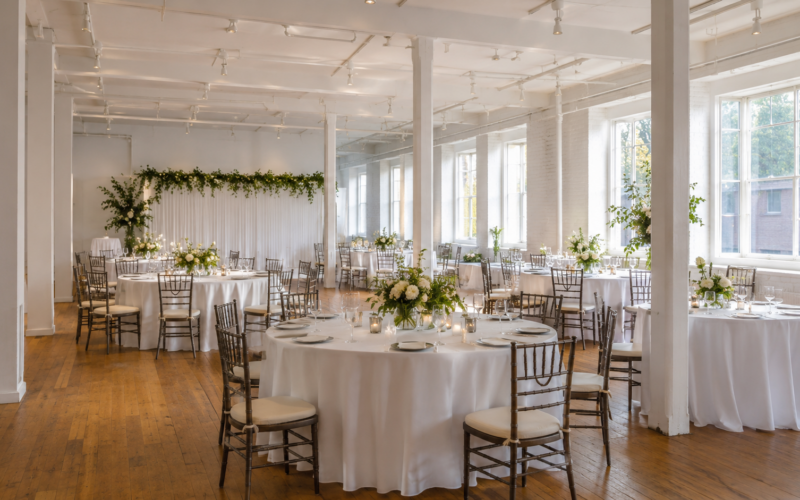 Helle Eventlocation mit gedeckten runden Tischen, Blumen und natürlichem Licht