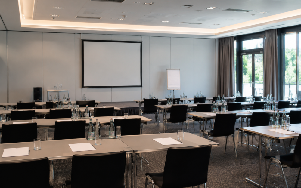 Moderner Tagungsraum mit Tischen, Stühlen, Leinwand und Präsentationstechnik